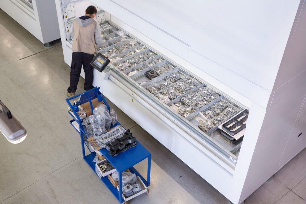 Operator retrieving electronic components from a vertical lift module with organized trays in an automated storage system.